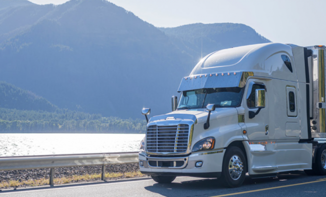 white semi truck driving down scenic highway through the mountains